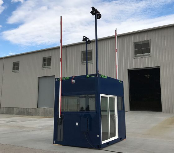 Vehicular security gatehouse features two barriers and light towers for increased visibility at night.
